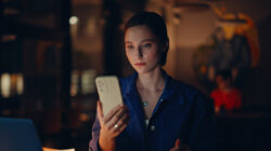 Joyful student browsing mobile phone message at dark workplace light closeup.