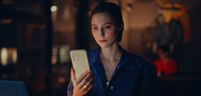Joyful student browsing mobile phone message at dark workplace light closeup.