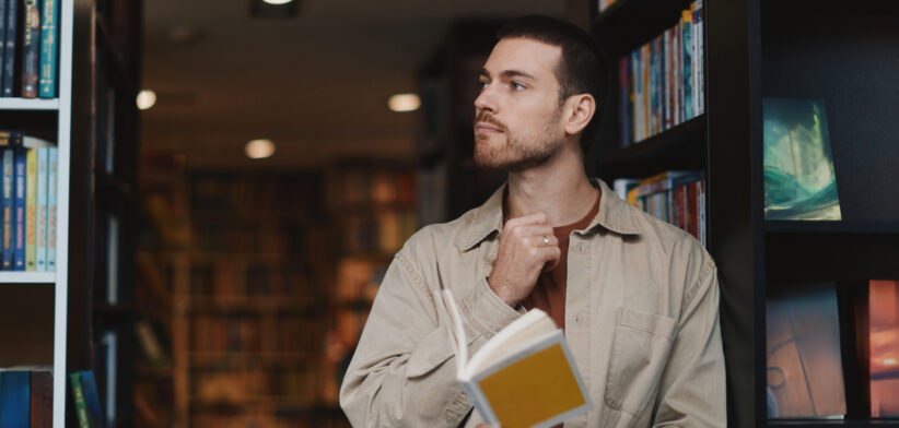Happy Adult Man Reading a Yellow Book in a Cozy Library, Smiling Casual Moment