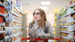 Bored woman leaning on shopping cart in supermarket holding grocery list