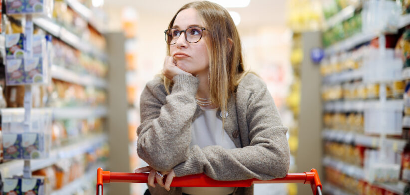 Bored woman leaning on shopping cart in supermarket holding grocery list