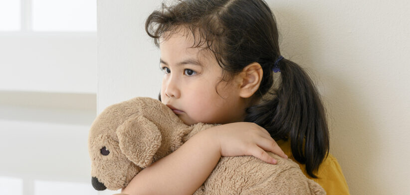 Little Asian girl stays home bored by school closings due to covid pandemic. Preschool girl looking outside her home window.