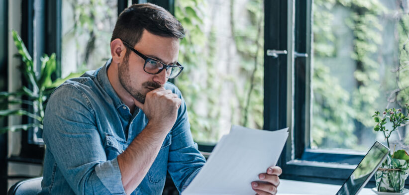 Worried businessman analyzing documents while working on laptop at table