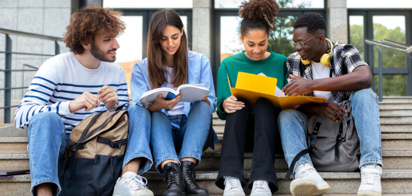 Happy diverse university student friends doing homework together sitting on campus steps.