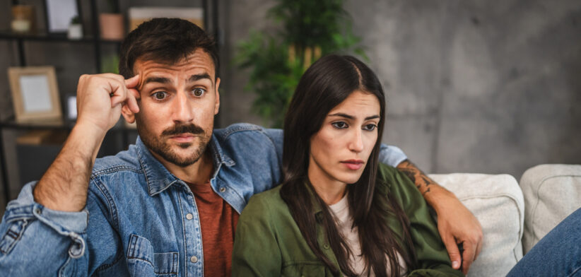 upset adult couple watch scary movie on television
