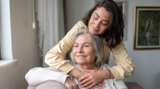 Daughter Hugging Senior Mother From Behind Holding Hands
