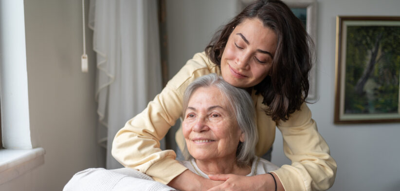 Daughter Hugging Senior Mother From Behind Holding Hands