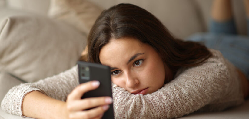 Woman checking phone lying on a couch in a house