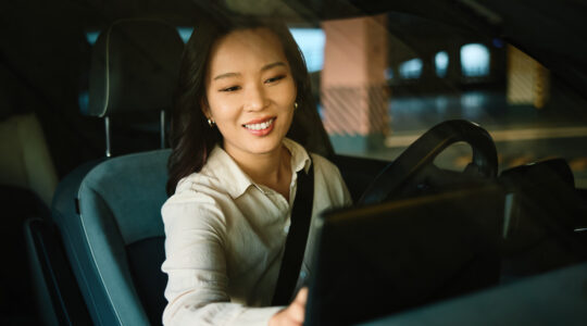 Woman driving modern electric car interacting with touchscreen