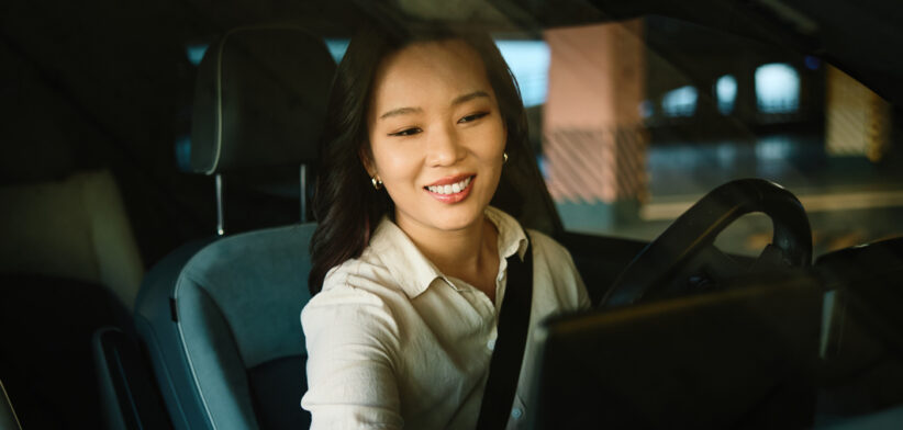 Woman driving modern electric car interacting with touchscreen