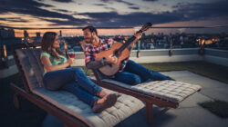 Romantic couple spending an evening with acoustic guitar and wine on a penthouse balcony.