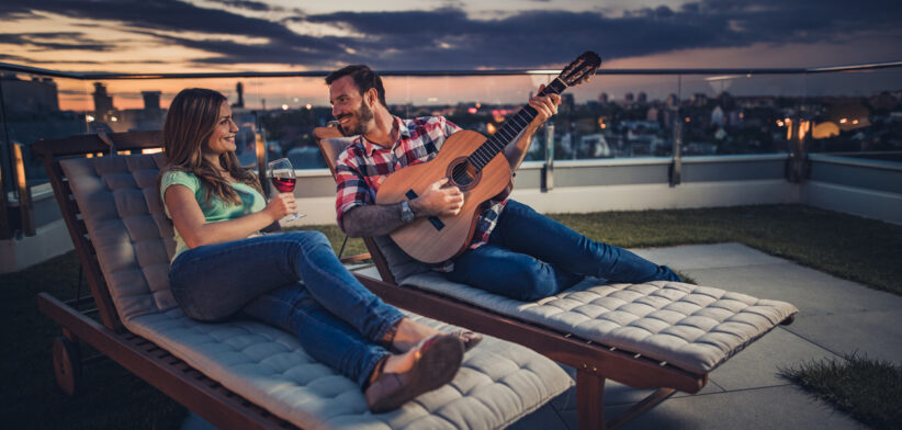 Romantic couple spending an evening with acoustic guitar and wine on a penthouse balcony.