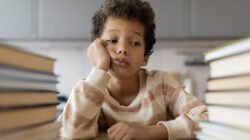 Bored black boy resting head on hand and looking at book stacks