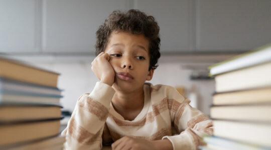 Bored black boy resting head on hand and looking at book stacks