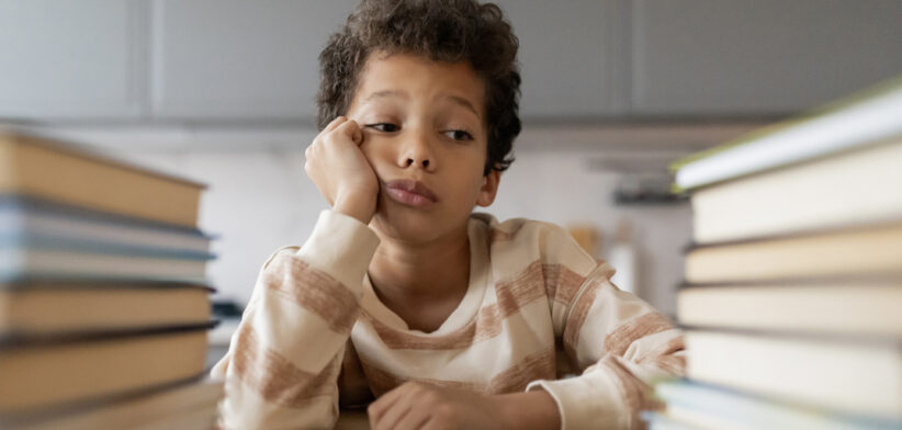 Bored black boy resting head on hand and looking at book stacks