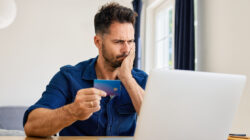 Frustrated man looking on laptop while paying with credit card