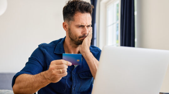 Frustrated man looking on laptop while paying with credit card