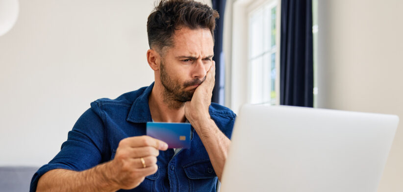 Frustrated man looking on laptop while paying with credit card
