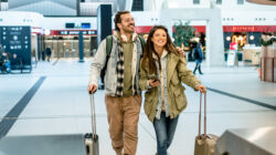 Happy tourists couple walking with luggage in airport terminal