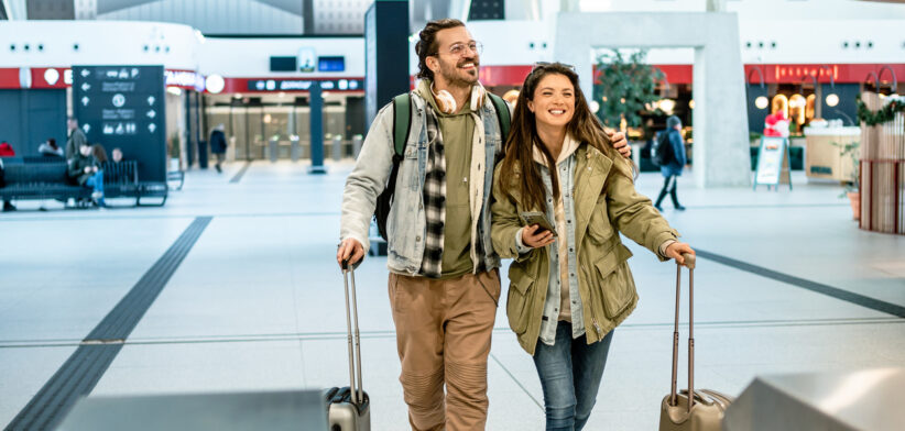 Happy tourists couple walking with luggage in airport terminal