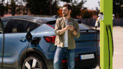 Man charging electric car and using smartphone at charging station