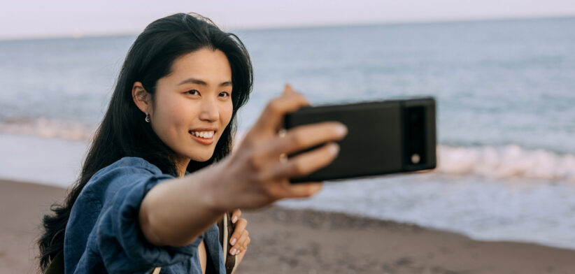 Chinese woman takes selfie on a sunny beach in Spain with beautiful sea and sand in background