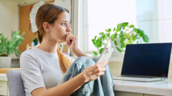 Upset sad young female sitting at home with smartphone