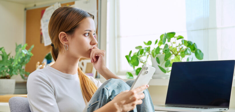 Upset sad young female sitting at home with smartphone