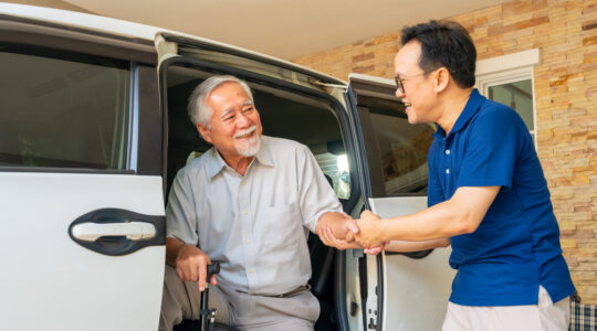 Caregiver helping senior man get in the car.