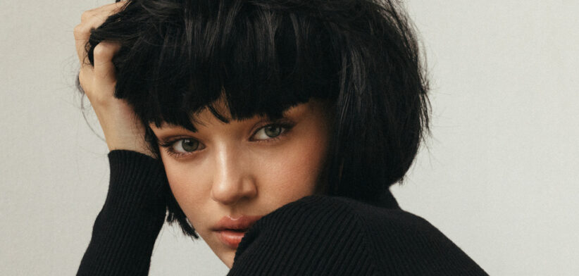 Portrait of a young woman with short black hair in a black knit sweater, conveying introspection