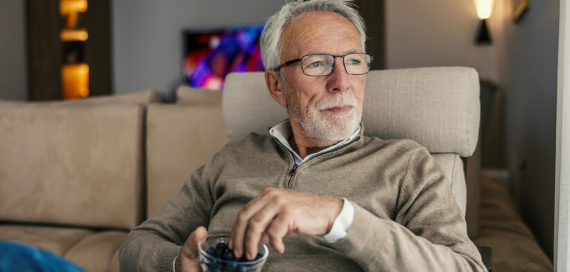 Senior man relaxing at home eating blueberries